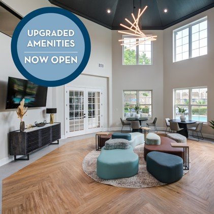 A community lounge with hardwood-style flooring, large windows with views of the swimming pool, vaulted ceilings, chairs, tables,  a TV, and upgraded amenities at Kensington by the Vineyard.